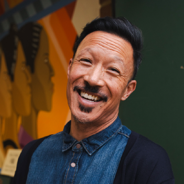 portrait of smiling asian american man with facial hair in front of mural